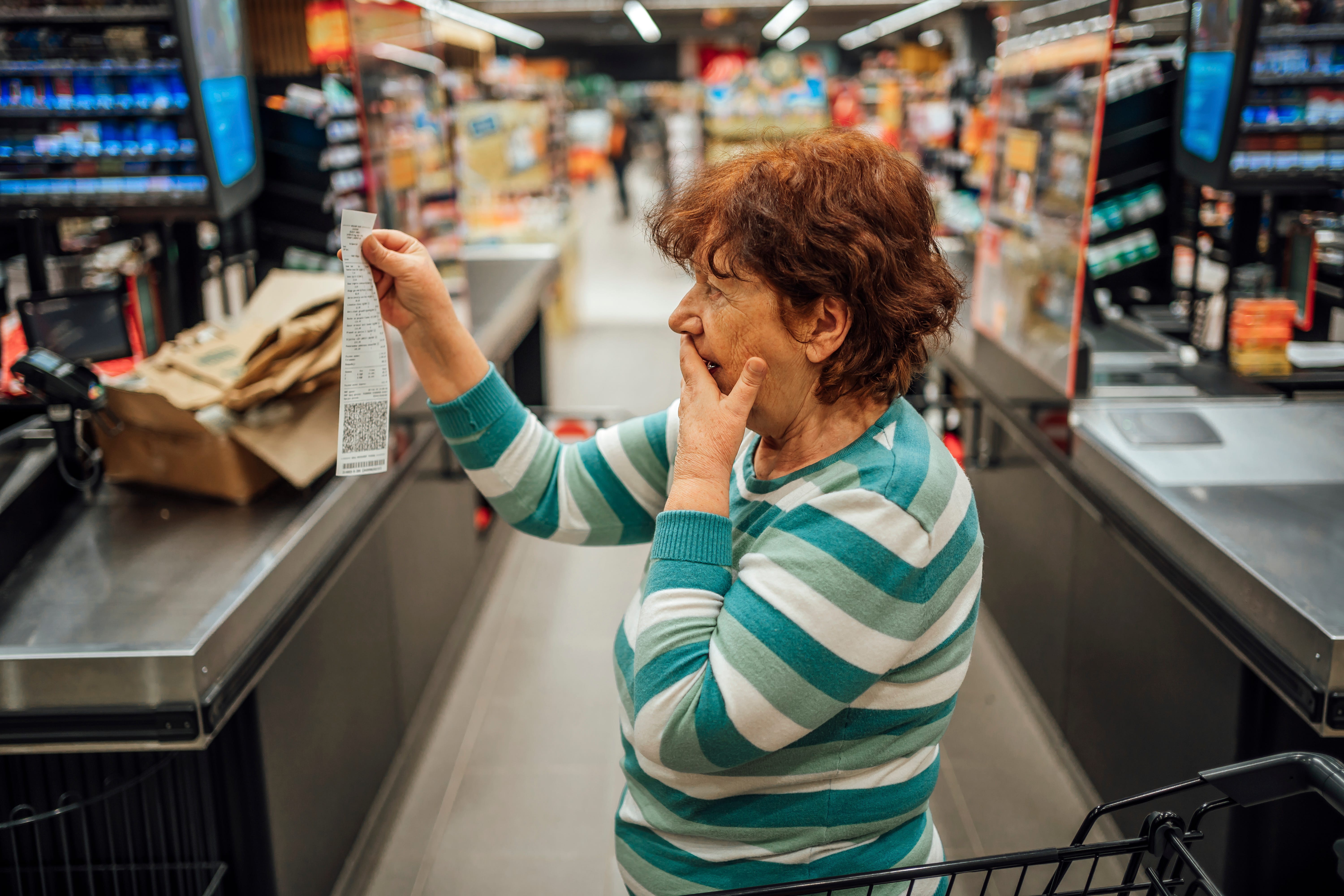 An elderly woman looks at a large receipt on a grocery store.