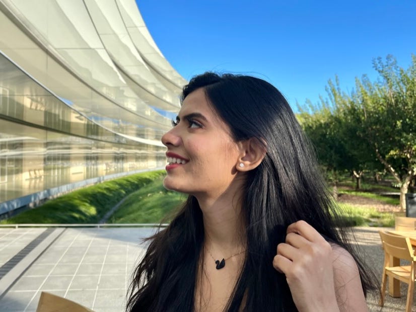 a woman with long dark hair, smiling and looking off the the left while standing outside