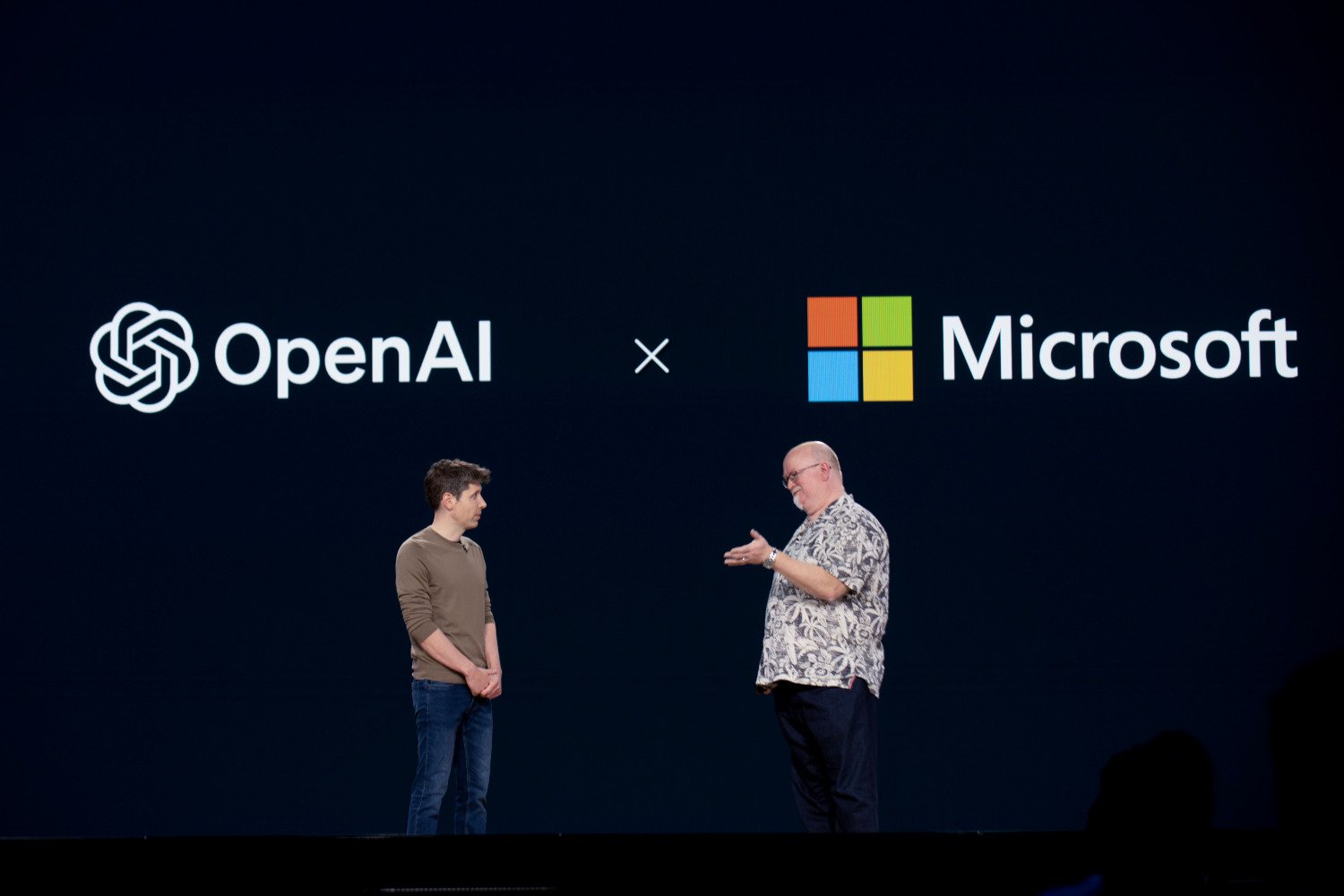 Kevin Scott, executive vice president of AI and chief technology officer of Microsoft appears on stage right under the Microsoft logo, and Sam Altman, chief executive officer of OpenAI, appears on stage to the left under the OpenAI logo