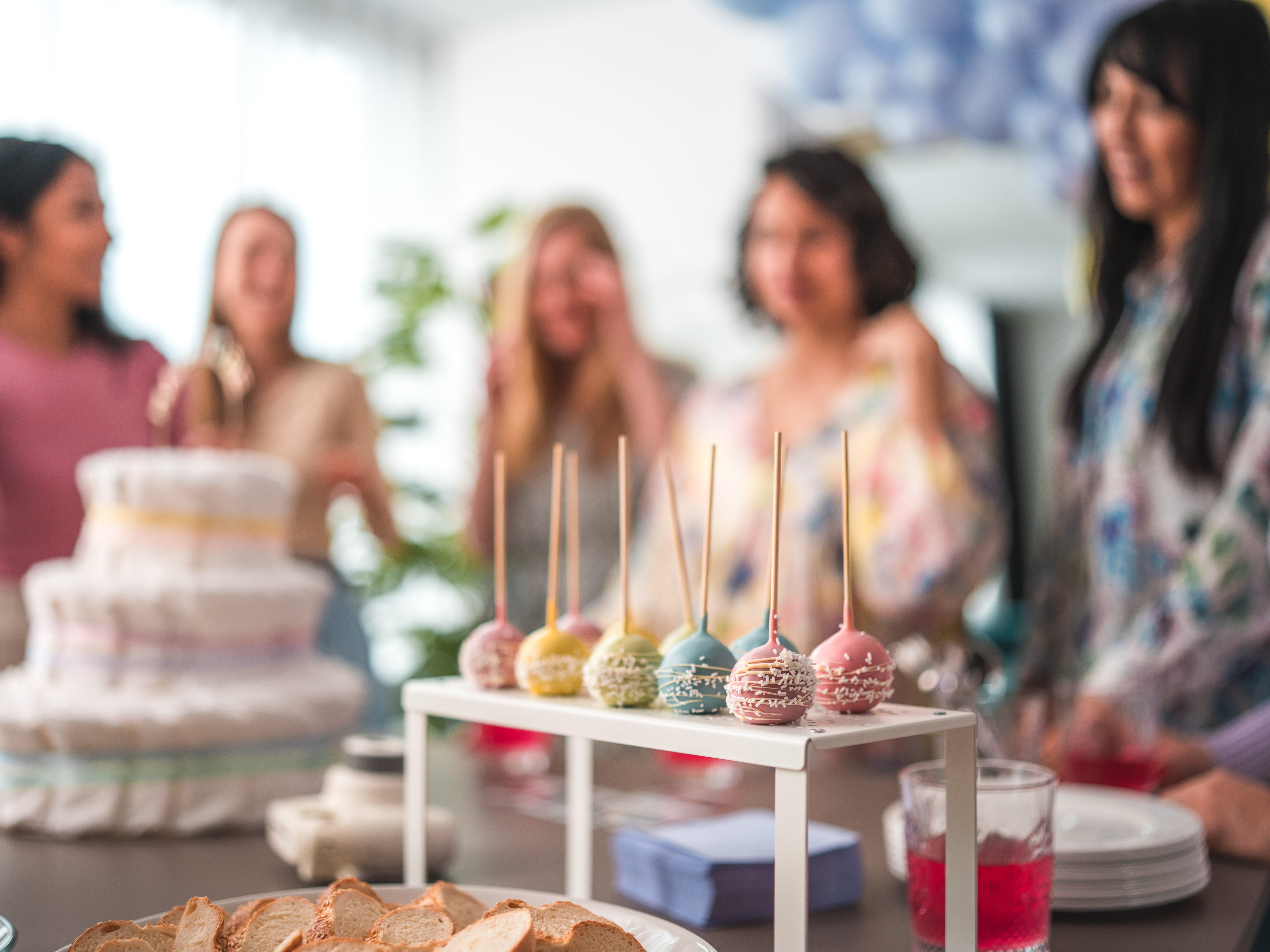A table with treats on it surrounded by people celebrating a baby shower.