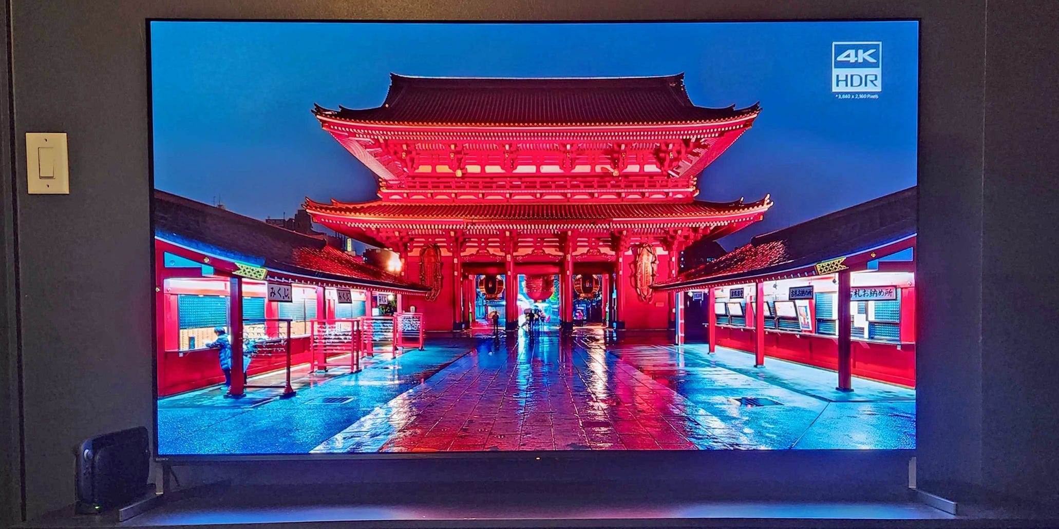 A Sony Bravia 8 II OLED TV on a media console with a video of a street in Japan at night playing on the screen.