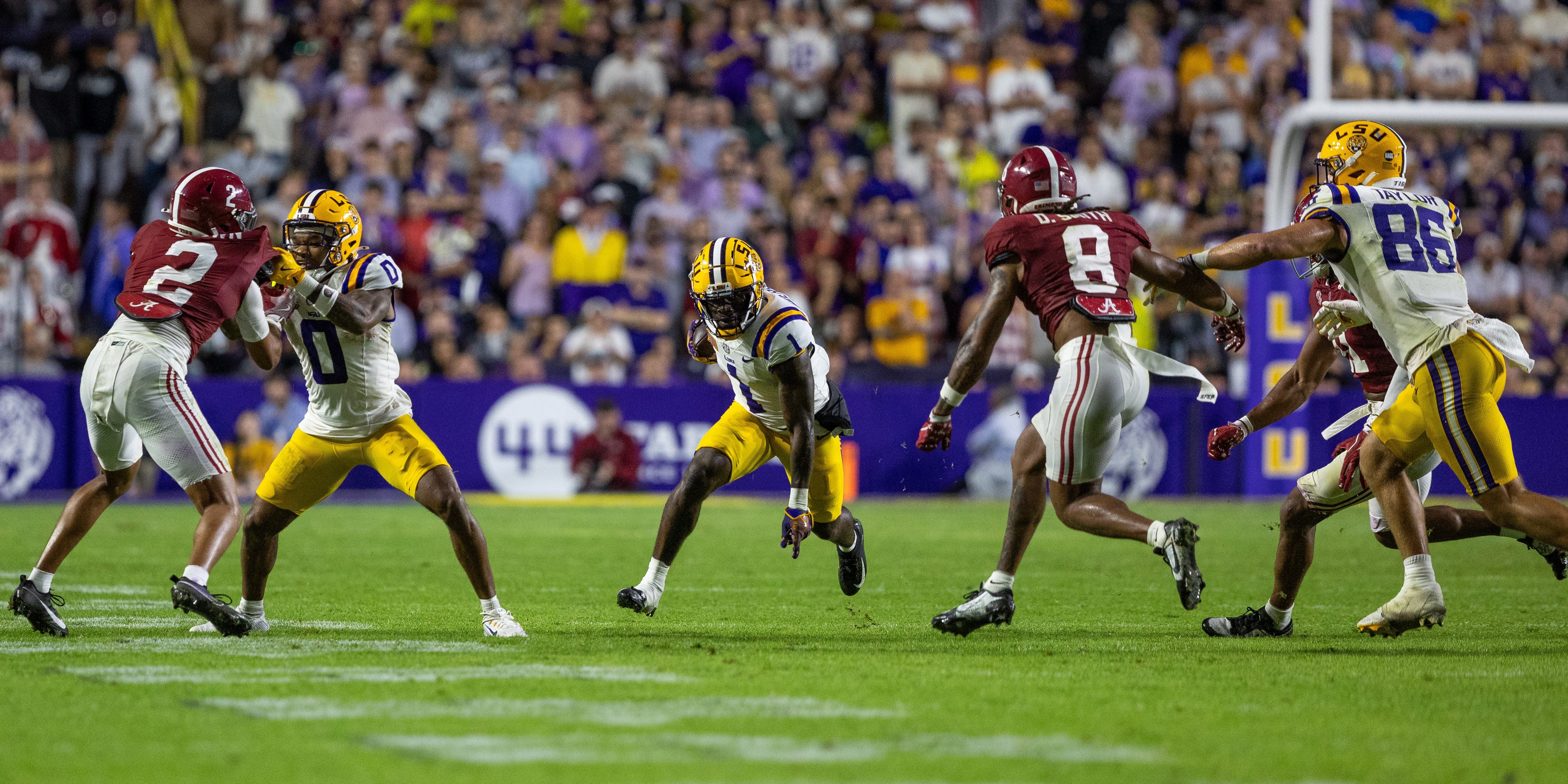 LSU and Alabama college football players clash during a 2024 game while Aaron Anderson runs up the field with the football.