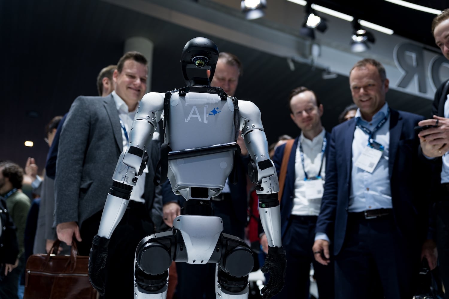 Excited lanyard guys at a trade show smile at a Unitree humanoid robot