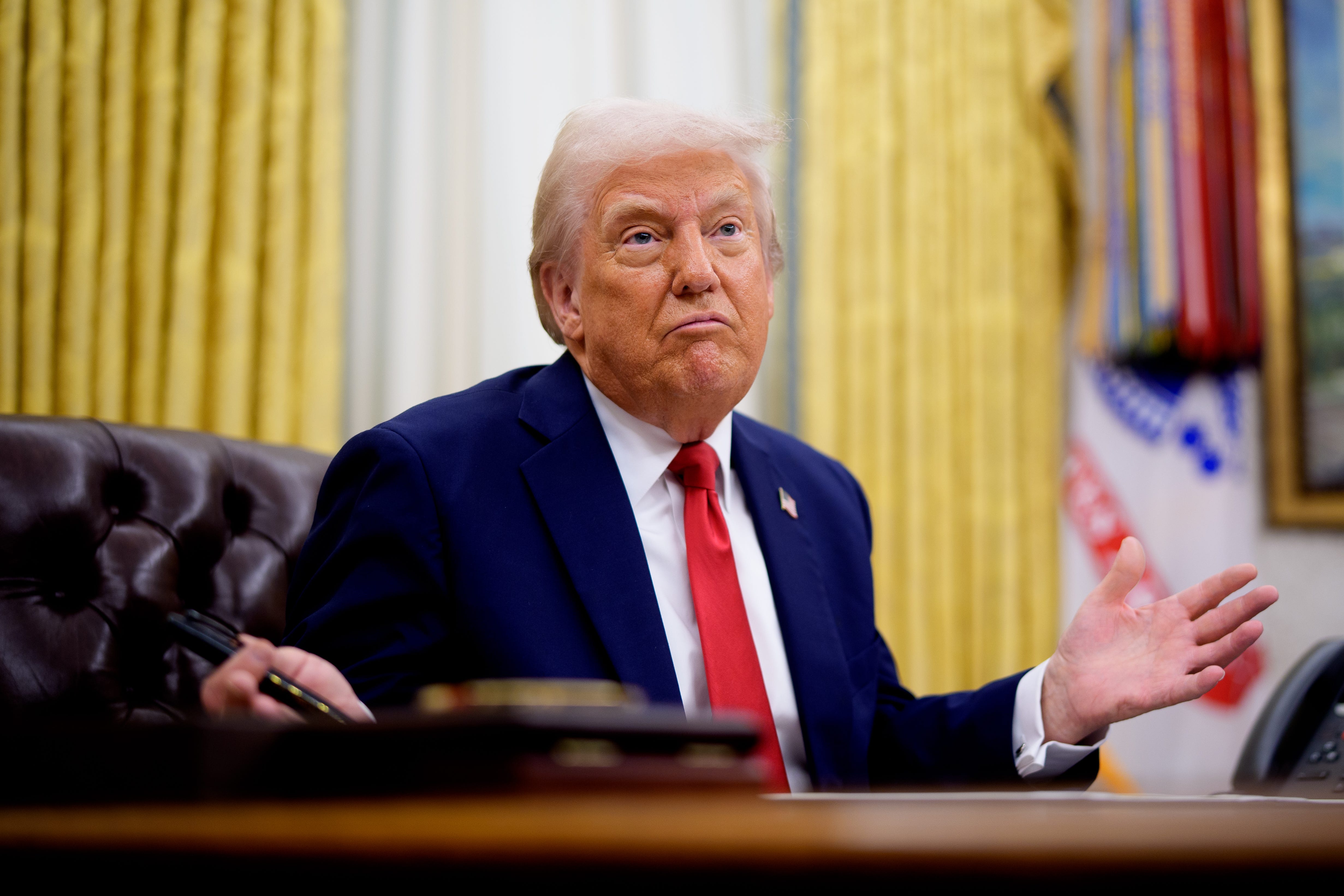 President Donald Trump gesturing his arms out while sitting in the Oval Office