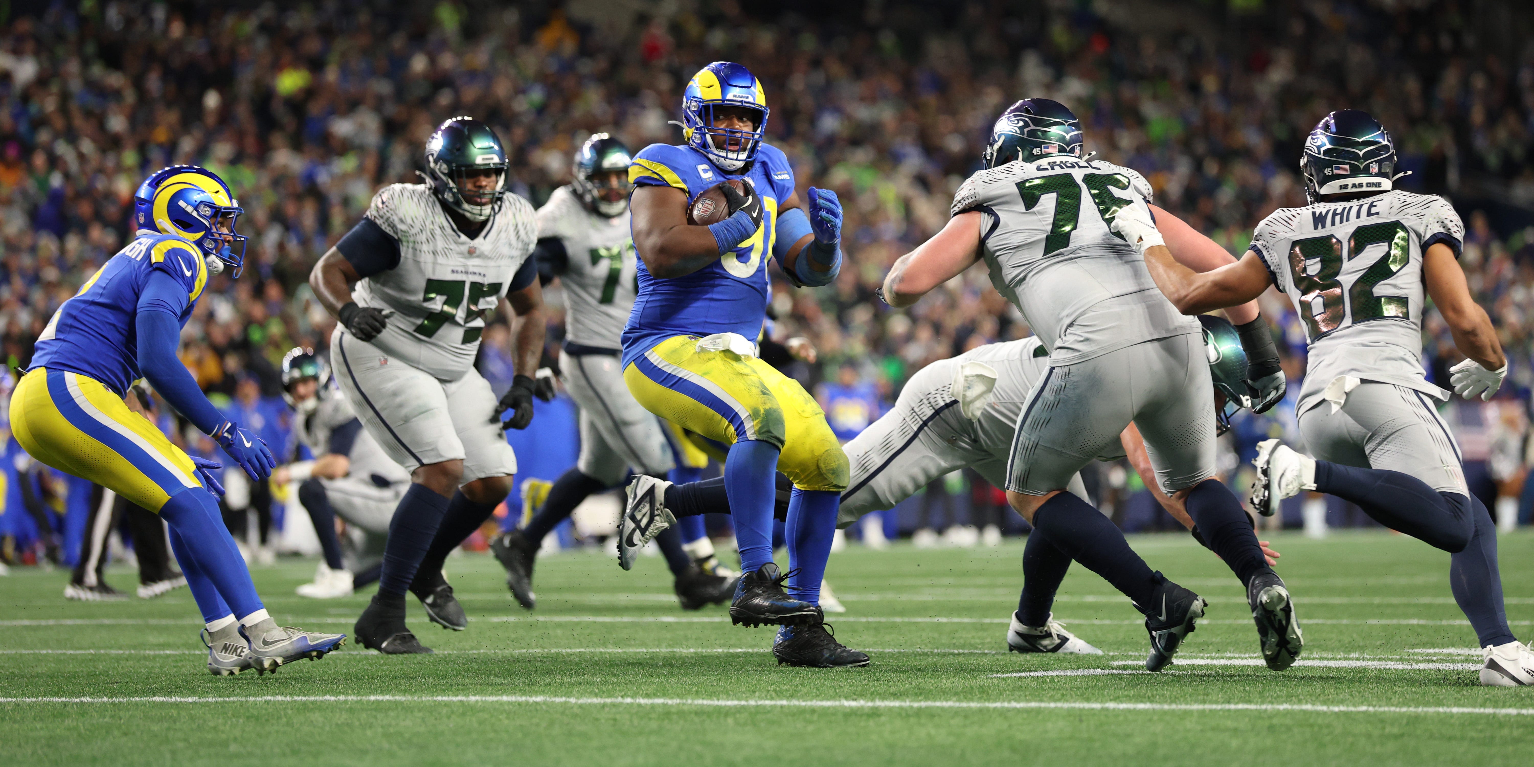 Kobie Turner #91 of the Los Angeles Rams looks on after an interception while Seattle Seahawks players run around him during a 2025 NFL game.