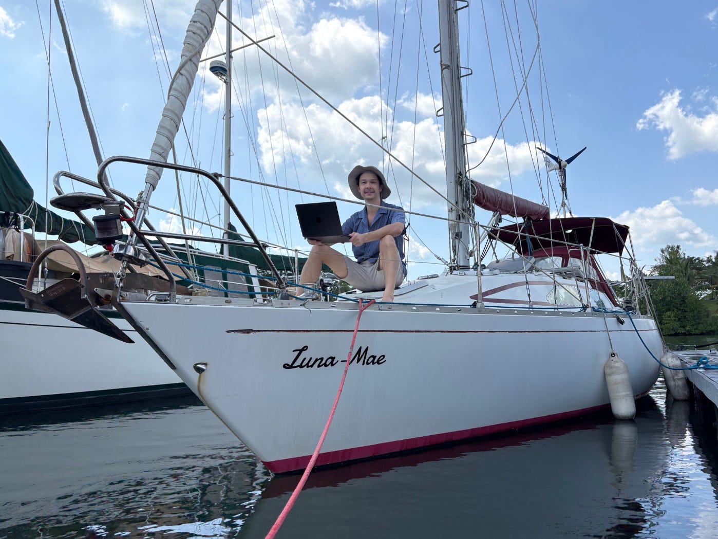 Jeremy Brand Yuan sitting on his boat holding a laptop. The name of the boat, "Luna Mae" is written on the side of the vessel.
