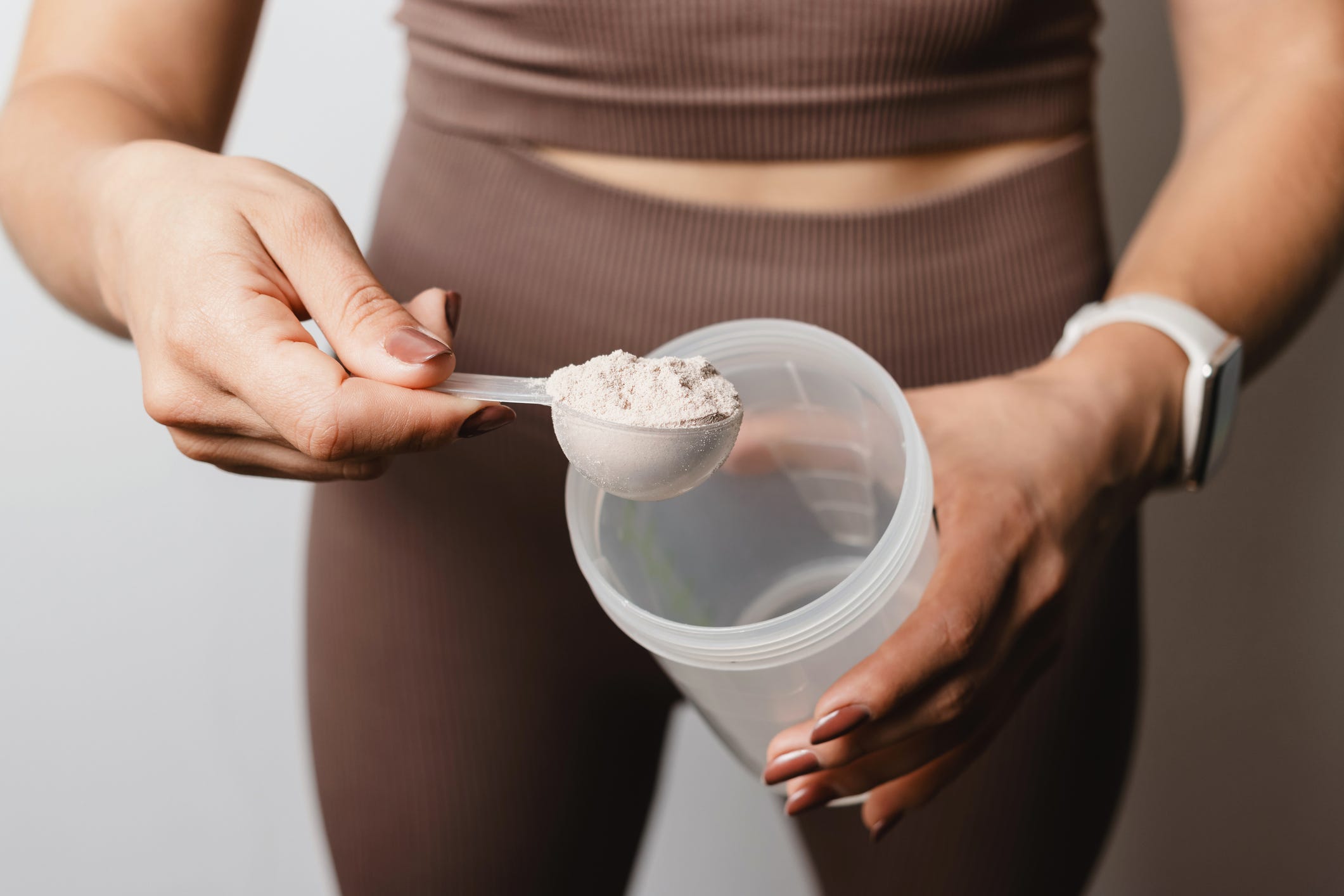 A person scooping a supplement powder into a clear plastic cup.