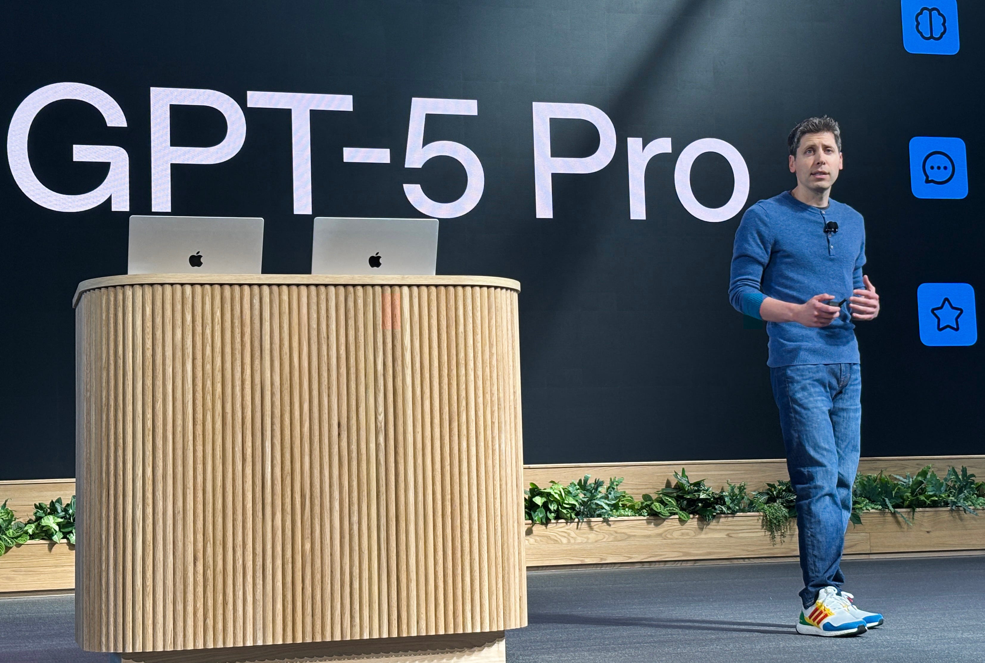 Sam Altman standing on stage at DevDay, wearing a blue shirt and jeans.