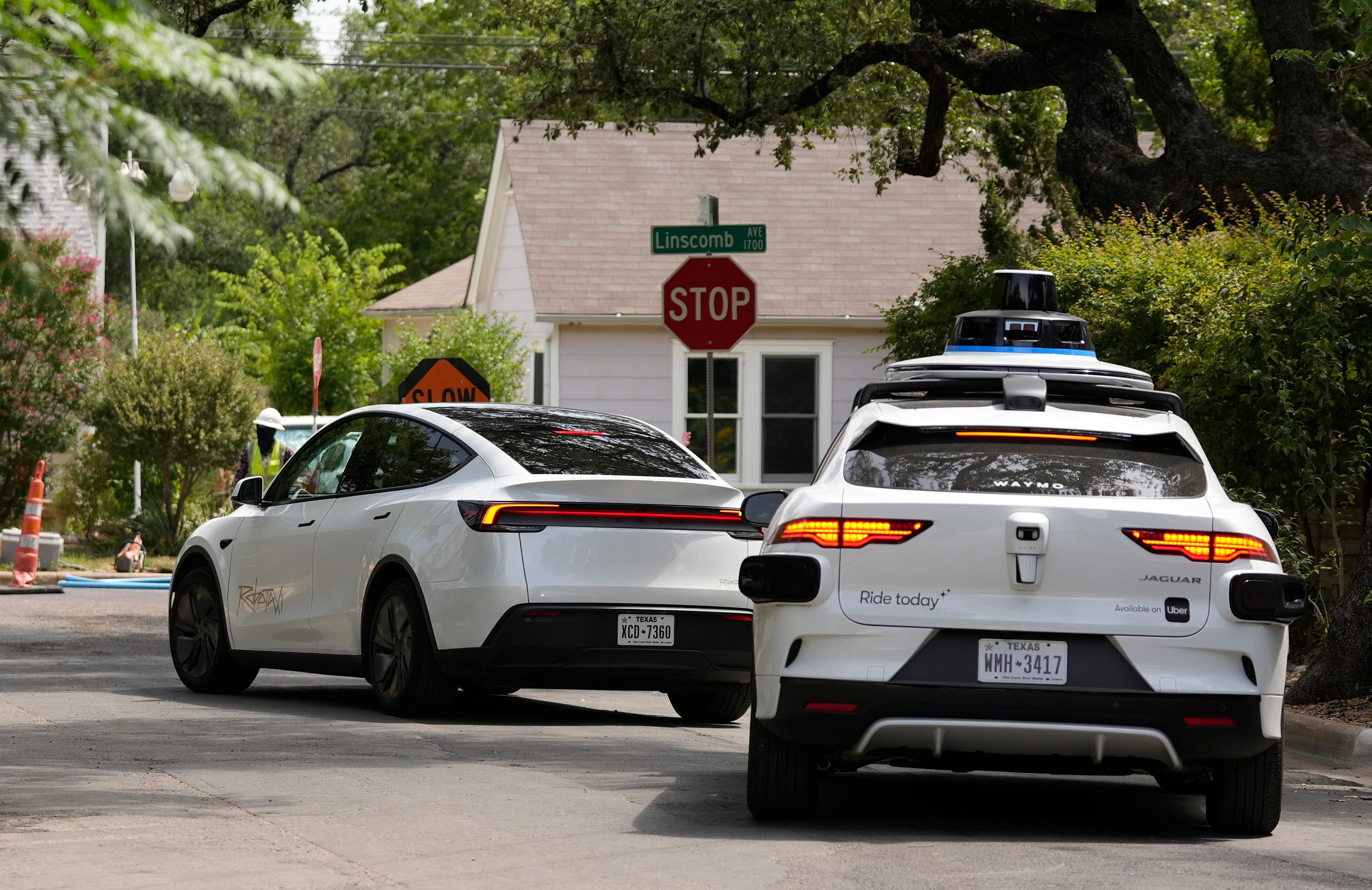 A Tesla Robotaxi stops at a stop sign. A Waymo follows.