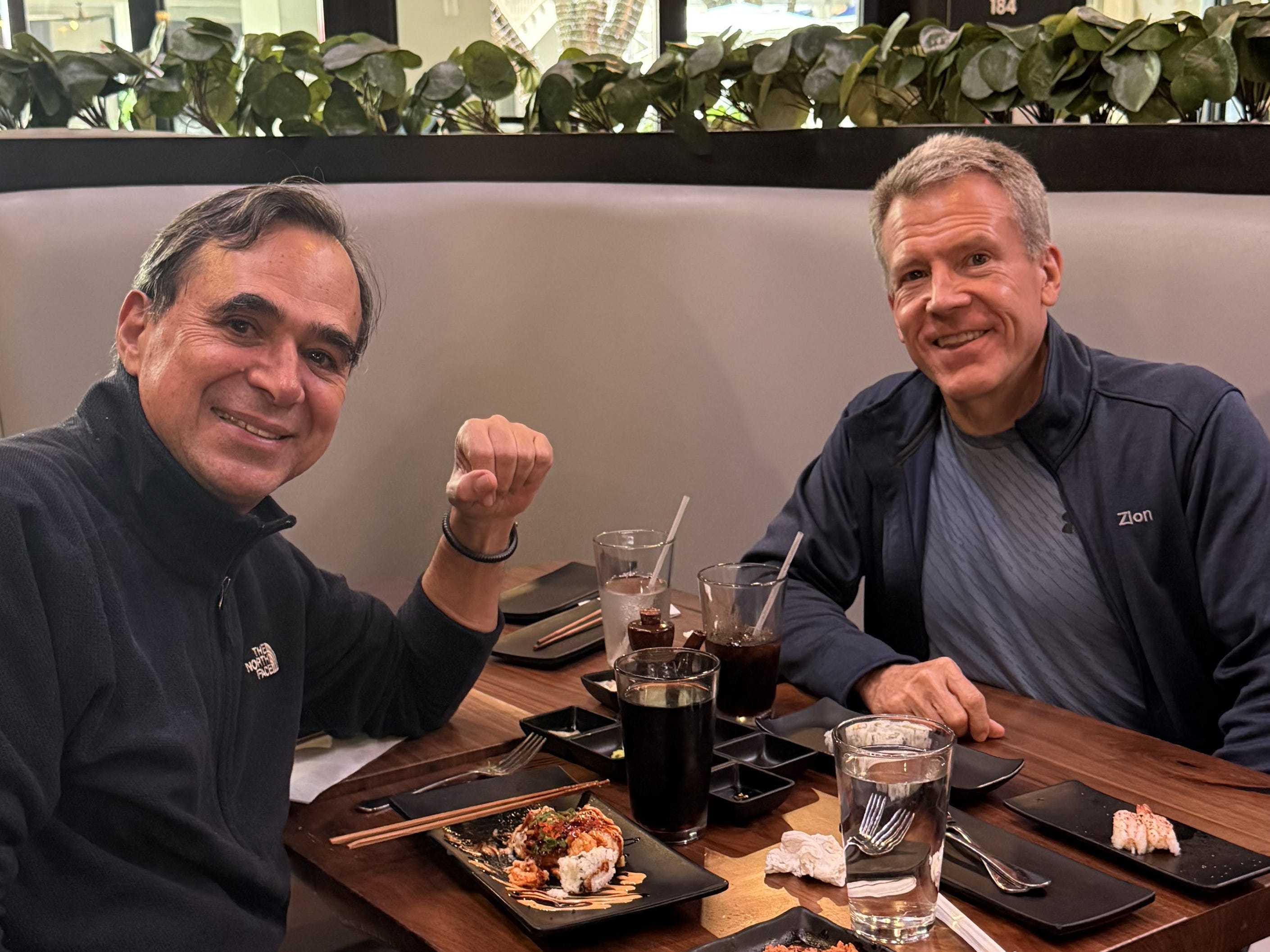 Scott Scovel and his friend Bruno are sitting down at a table for lunch. On the table there's some sushi on plates and drink glasses.