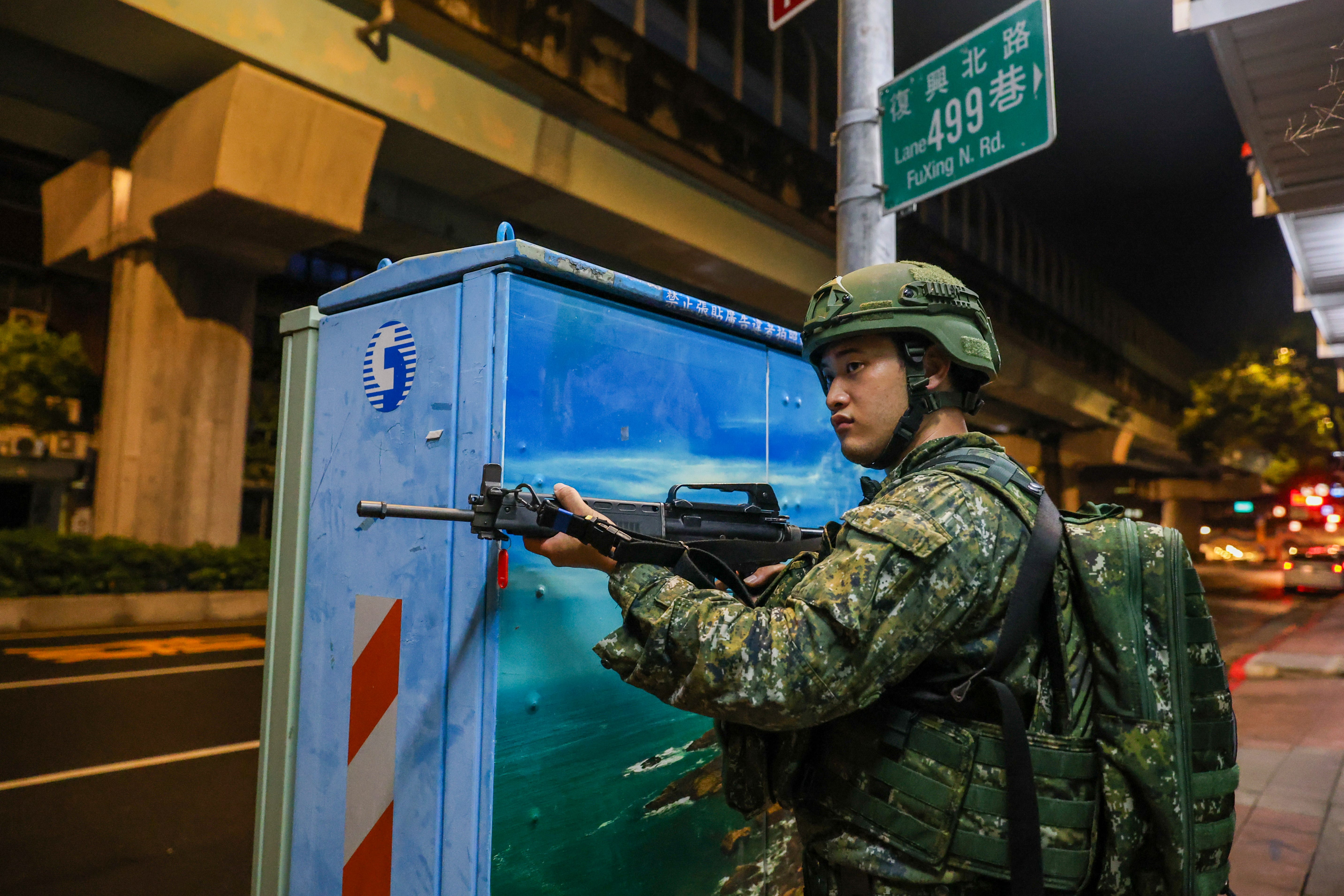 A Taiwanese soldier stands guard on a road next to an electrical fusebox.